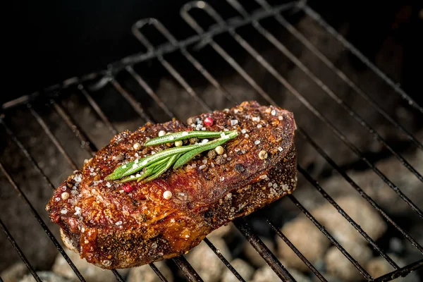 Bife picante quente grelhando em um churrasco de verão sobre as brasas quentes decoradas com um ramo de alecrim — Fotografia de Stock