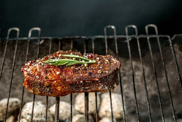 Bife picante quente grelhando em um churrasco de verão sobre as brasas quentes decoradas com um ramo de alecrim — Fotografia de Stock