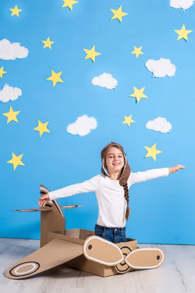 Piccola sognatrice che gioca con un aeroplano di cartone allo studio con cielo blu e sfondo di nuvole bianche . — Foto Stock