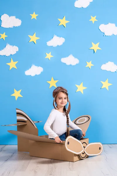 Piccola sognatrice che gioca con un aeroplano di cartone allo studio con cielo blu e sfondo di nuvole bianche . — Foto Stock