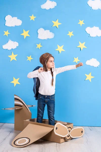 Piccola sognatrice che gioca con un aeroplano di cartone allo studio con cielo blu e sfondo di nuvole bianche . — Foto Stock