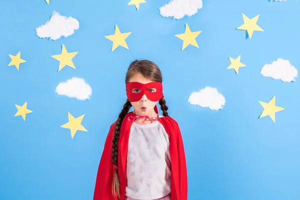 Маленька дитина грає в супергероя. Малюк на тлі яскраво-блакитної стіни з білими хмарами та зірками. Концепція влади дівчини . — стокове фото