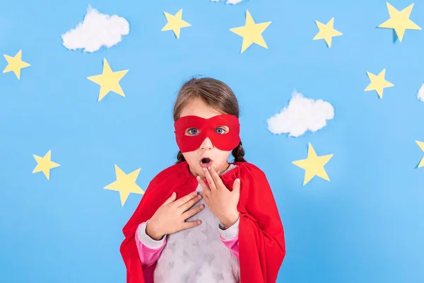 Маленька дитина грає в супергероя. Малюк на тлі яскраво-блакитної стіни з білими хмарами та зірками. Концепція влади дівчини . — стокове фото
