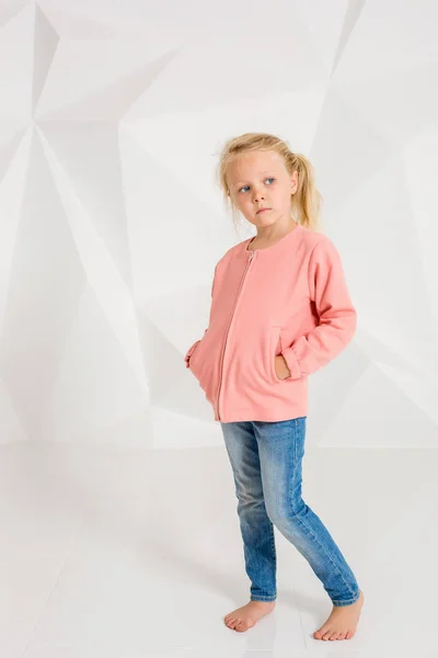 Aranyos kis lány, pink dzseki és farmer, kezek a zsebek, fehér háttér — Stock Fotó
