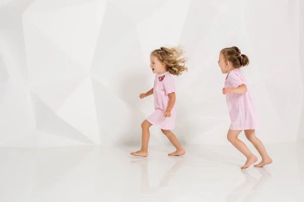 Két kis vicces, és nevetve a lány óvatosan rózsaszín ruha fehér stúdióban játszik — Stock Fotó