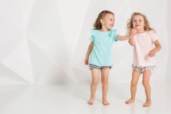 Két kis vicces, és nevetve a lány az azonos ruhát a különböző színek a fehér stúdió játék — Stock Fotó