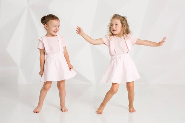 Két kis vicces, és nevetve a lány óvatosan rózsaszín ruha fehér stúdió pózol — Stock Fotó