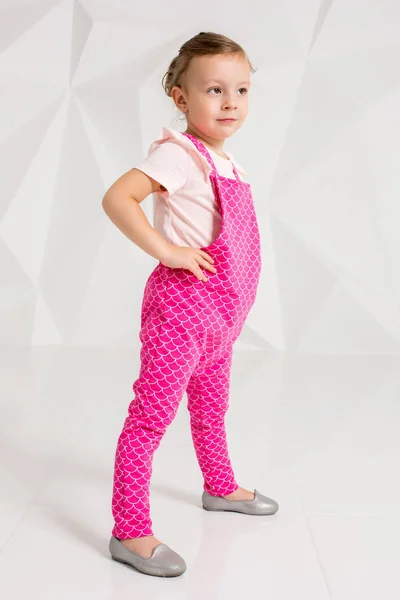 Beautiful little girl with blond hair, in pink overalls on white background — Stock Photo, Image