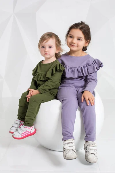 Děti, dvě sestry 1,5 a 5 let v identické kostýmy různých barev, malé holčičky na bílém pozadí v ateliéru — Stock fotografie