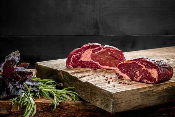 Čerstvé syrové hovězí maso na prkénku s čerstvou bazalkou a rozmarýnem — Stock fotografie