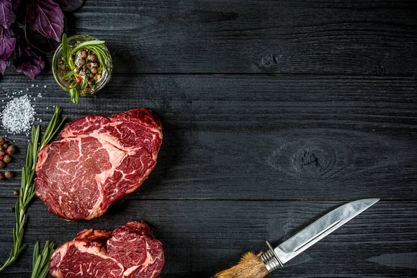 Fesleğen ve rosemary ile siyah ahşap zemin üzerine Ahşap Saplı bıçak sapı ile taze çiğ et. Üstten Görünüm