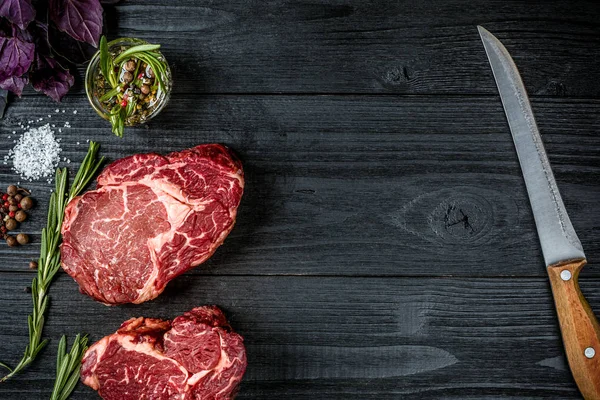 Fesleğen ve rosemary ile siyah ahşap zemin üzerine Ahşap Saplı bıçak sapı ile taze çiğ et. Üstten Görünüm