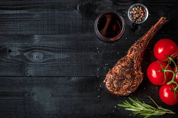 Grill trocken gereifte Rinderrippe mit Gewürzen, Gemüse und einem Glas Rotwein in Großaufnahme auf schwarzem Holzhintergrund — Stockfoto