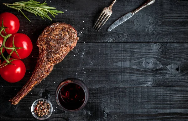 Suché věku žebra grilování hovězího masa s kořením, zeleninou a Sklenka červeného vína close-up na černém pozadí dřevěná — Stock fotografie
