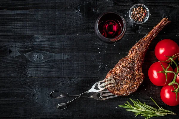 Barbacoa costilla seca envejecida de ternera con especias, verduras y copa de vino tinto de cerca sobre fondo de madera negro — Foto de Stock