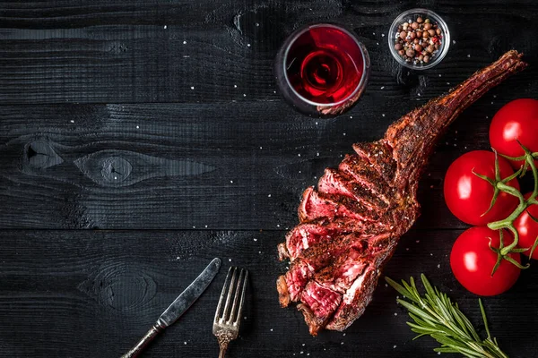 Grill trocken gereifte Rinderrippe mit Gewürzen, Gemüse und einem Glas Rotwein in Großaufnahme auf schwarzem Holzhintergrund — Stockfoto
