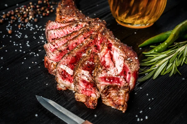 Barbecue droge leeftijd rib van rundvlees met kruiden, groenten en een glas light bier close-up op zwarte houten achtergrond — Stockfoto