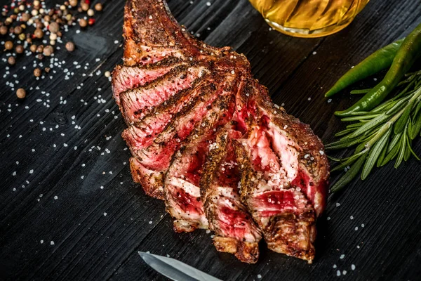 Suché věku žebra grilování hovězího masa s kořením, zeleninou a sklenku světlé pivo close-up na černém pozadí dřevěná — Stock fotografie