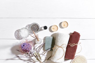 Spa Ürünleri. Banyo tuzları, kuru çiçekler lavanta, sabun, mumlar ve havlu. Düz beyaz ahşap zemin, üstten görünüm üzerinde yatıyordu.