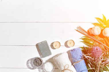 Spa Ürünleri. Banyo tuzları, kuru çiçekler lavanta, sabun, mumlar ve havlu. Düz beyaz ahşap zemin, üstten görünüm üzerinde yatıyordu. Güneş parlaması