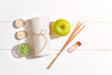 Spa Ürünleri. Banyo tuzları, sabun, mumlar ve havlu. Düz beyaz ahşap zemin, üstten görünüm üzerinde yatıyordu. Güneş parlaması