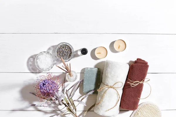 Spa Ürünleri. Banyo tuzları, kuru çiçekler lavanta, sabun, mumlar ve havlu. Düz beyaz ahşap zemin, üstten görünüm üzerinde yatıyordu.