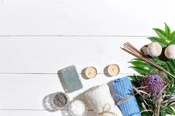 Spa Ürünleri. Banyo tuzları, kuru çiçekler lavanta, sabun, mumlar ve havlu. Düz beyaz ahşap zemin, üstten görünüm üzerinde yatıyordu.