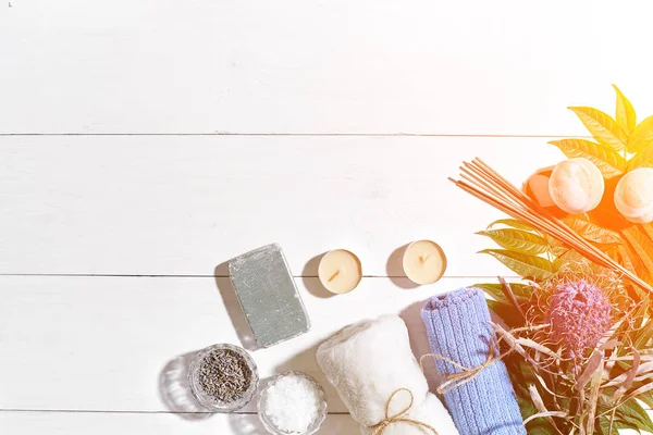 Spa Ürünleri. Banyo tuzları, kuru çiçekler lavanta, sabun, mumlar ve havlu. Düz beyaz ahşap zemin, üstten görünüm üzerinde yatıyordu. Güneş parlaması