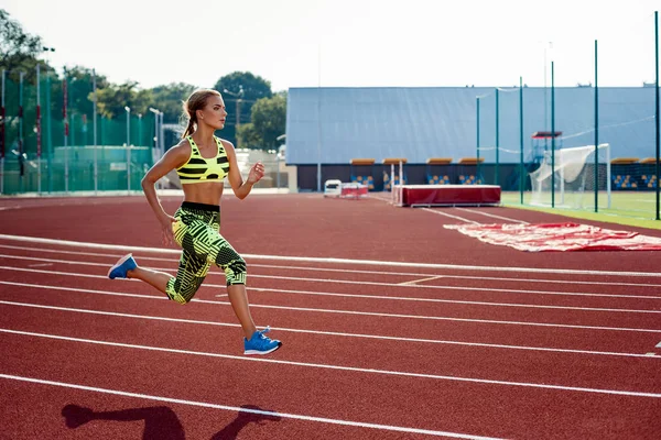 Koşu ve atletik yolda stadyum üzerinde çalışan güzel bir genç kadın egzersiz.