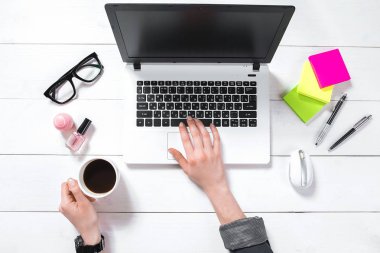 Beyaz ofis masaüstü kahve fincanı ile kadının el laptop tuş takımında yazarak üstten görünüm yerleştirilen.