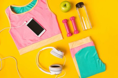 Spor donatımı ve giysileri ile sarı arka plan üstünde hareket eden telefon. Üstten Görünüm