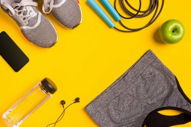 Sarı arka plan üzerinde Fitness aksesuarları. Spor ayakkabı, şişe su, kulaklık ve spor top.