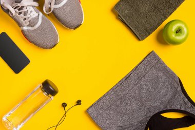 Sarı bir arka plan üzerinde Fitness aksesuarları. Spor ayakkabı, şişe su, elma ve spor top.