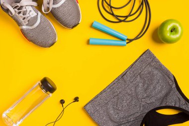 Sarı arka plan üzerinde Fitness aksesuarları. Spor ayakkabı, şişe su, kulaklık ve spor top.