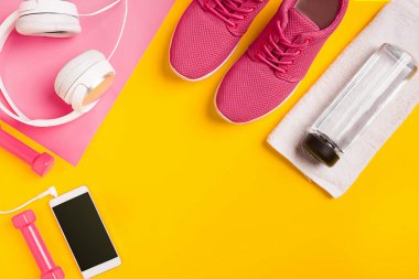 Sarı bir arka plan üzerinde Fitness aksesuarları. Spor ayakkabı, şişe su, kulaklık ve halter.