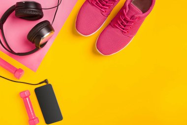 Sarı bir arka plan üzerinde Fitness aksesuarları. Spor ayakkabı, şişe su, kulaklık ve halter.