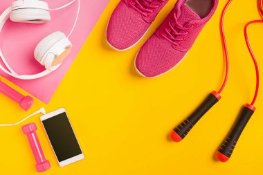 Sarı arka plan üzerinde Fitness aksesuarları. Spor ayakkabı, halter, kulaklık ve akıllı.