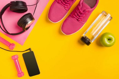 Sarı arka plan üzerinde Fitness aksesuarları. Spor ayakkabı, şişe su, kulaklık ve akıllı.