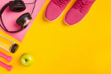 Sarı bir arka plan üzerinde Fitness aksesuarları. Spor ayakkabı, şişe su, kulaklık ve halter.