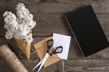Leylak çiçeği tablet tebrik mesajı için boş alan ile rustik ahşap arka plan üzerinde. Makas, iplik makarası, küçük zarf. Üstten Görünüm