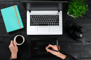 Bir fincan kahve tutarak ve siyah ahşap masa üstünde a laptop klavye yazarak eller.