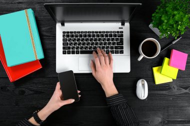 Bir akıllı tutarak ve siyah ahşap masa üstünde a laptop klavye yazarak eller.