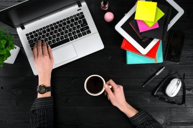 Bir fincan kahve tutarak ve siyah ahşap masa üstünde a laptop klavye yazarak eller.