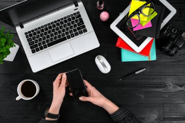 Bir akıllı tutarak ve siyah ahşap masa üstünde a laptop klavye yazarak eller.