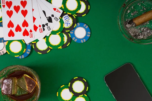 gambling, fortune and entertainment concept - close up of casino chips, whisky glass, playing cards and cigar on green table surface