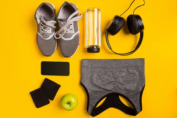 Accessoires de fitness sur fond jaune. Baskets, bouteille d'eau, casque et haut de sport . — Photo