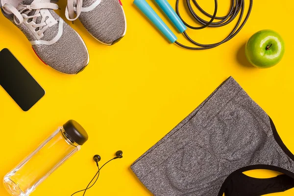 Fitness-Accessoires auf gelbem Hintergrund. Turnschuhe, Wasserflasche, Kopfhörer und Sporttop. — Stockfoto