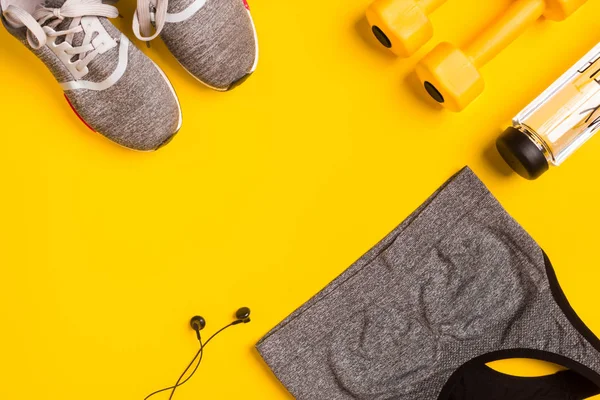 Fitness accessories on a yellow background. Sneakers, bottle of water, headphones and sport top.