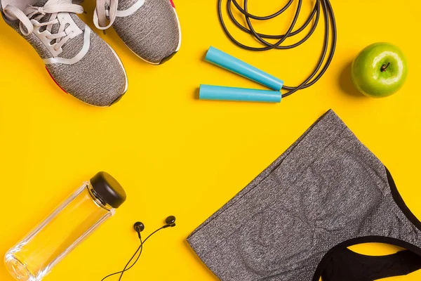 Sarı arka plan üzerinde Fitness aksesuarları. Spor ayakkabı, şişe su, kulaklık ve spor top.
