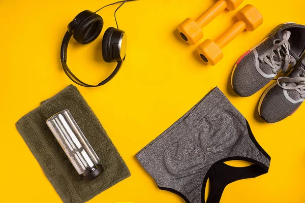 Fitness accessories on a yellow background. Sneakers, bottle of water, smart, towel and sport top.